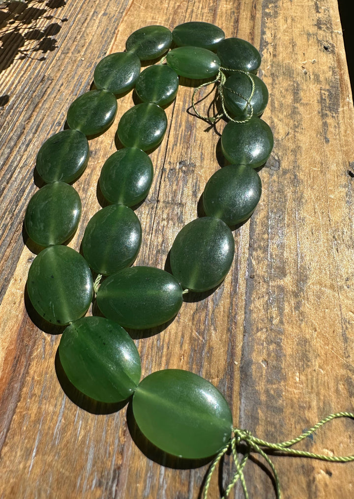 String of large oval green jade beads laid on a weathered wooden surface