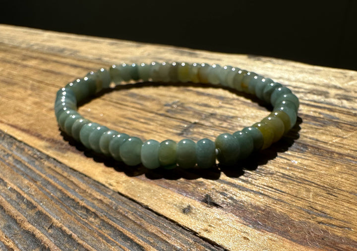 Close up of jadeite rondelle bead bracelet around a wrist on a wooden surface
