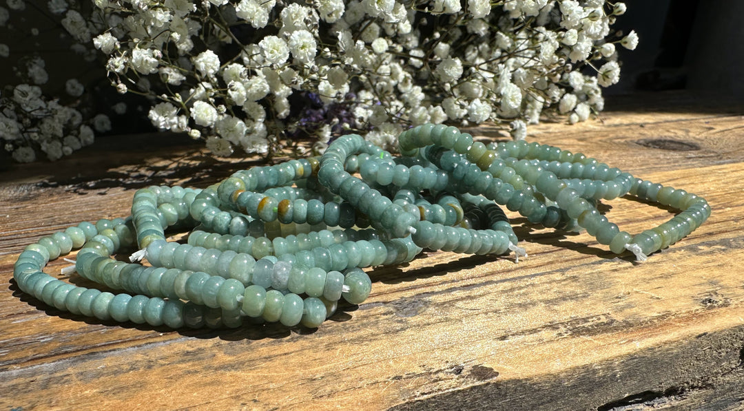 Guatemalan jadeite rondelle bead bracelets arranged on a weathered wooden surface with white baby&