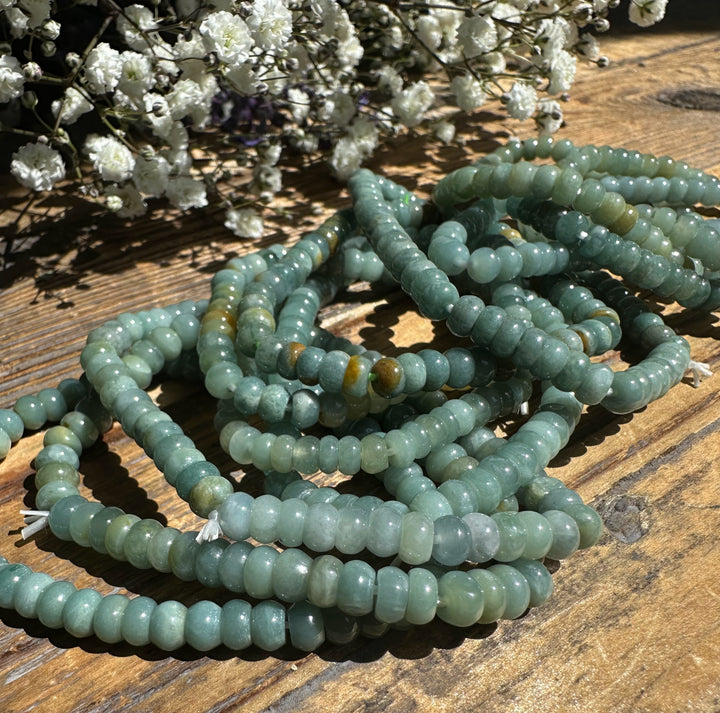 Guatemalan jadeite rondelle bead bracelets spread on a rustic wood surface in pale teal green tones
