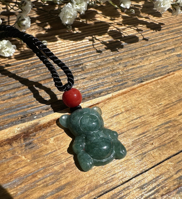 Close-up of a Guatemalan Jadeite Teddy Bear Pendant with red bead on a black cord