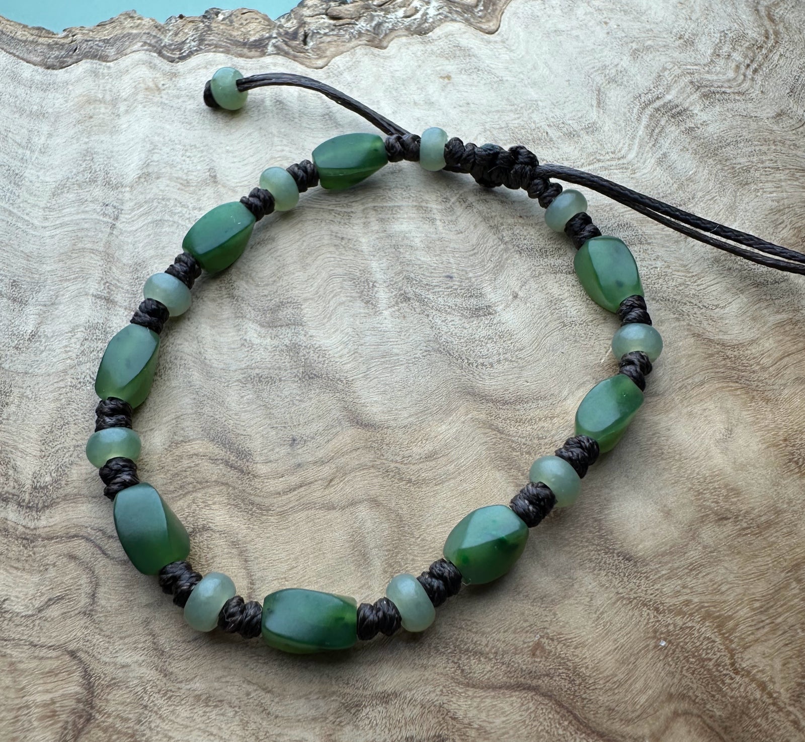 Green gemstone bracelet with oval and round beads on black braided cord and sliding knot.