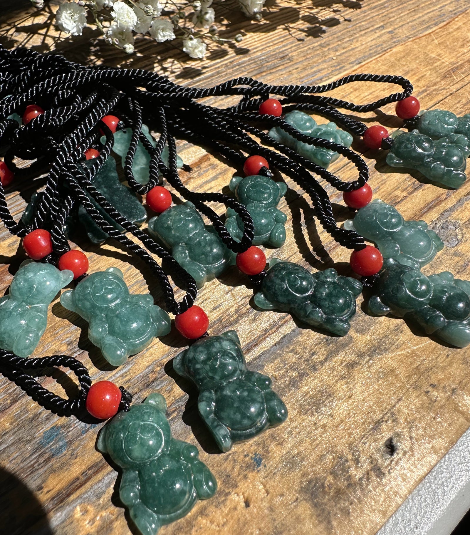 Guatemalan Jadeite Teddy Bear pendants on black cords with red beads spread across a wooden surface