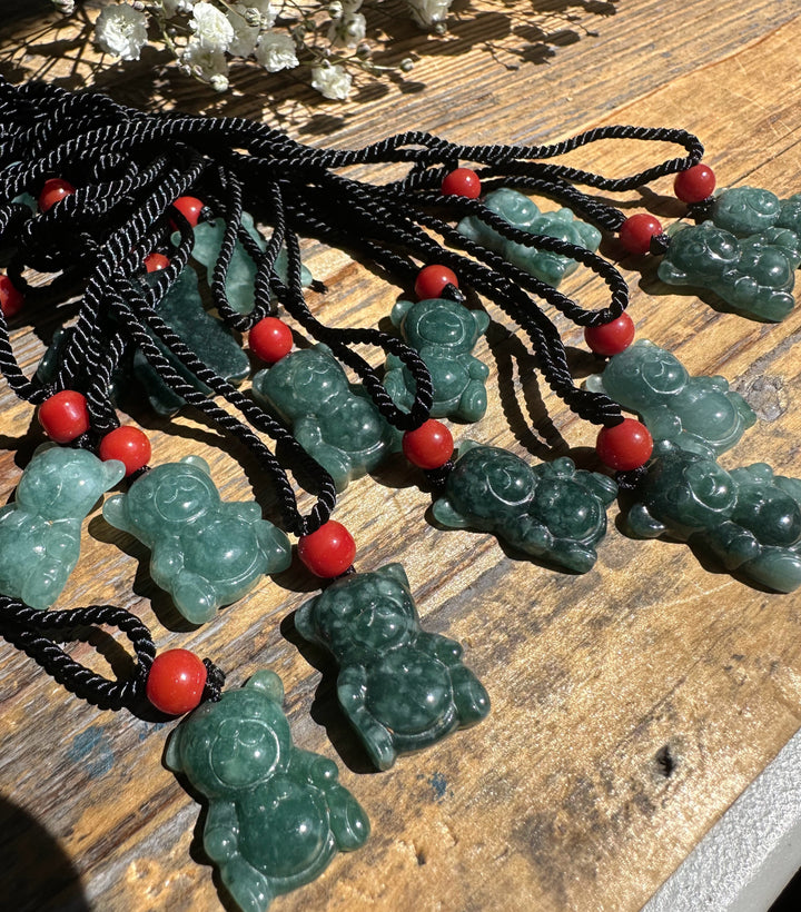 Guatemalan Jadeite Teddy Bear pendants on black cords with red beads spread across a wooden surface