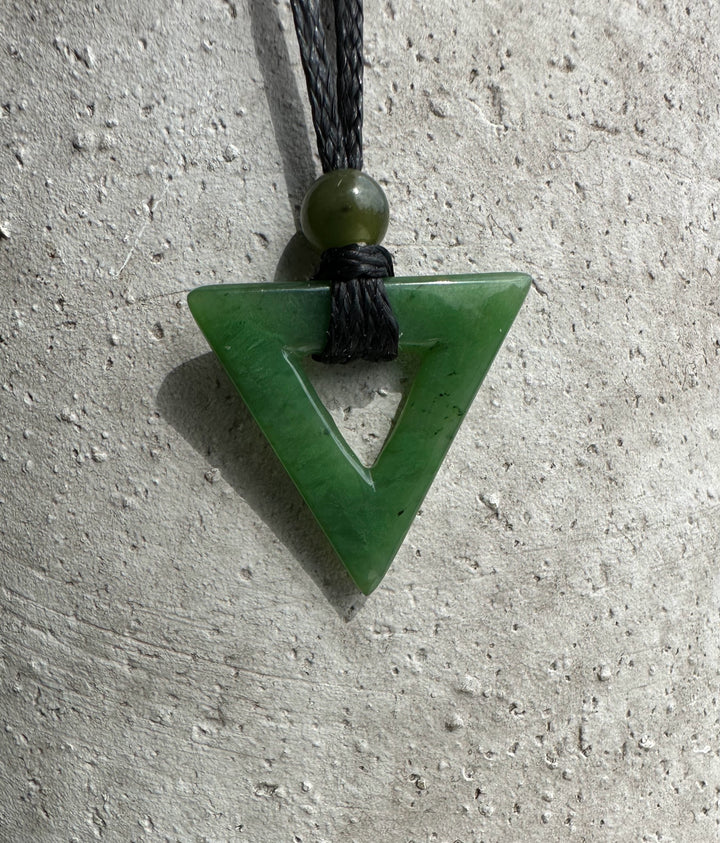 Green jade triangle pendant with hollow center on black cord and a round bead above.