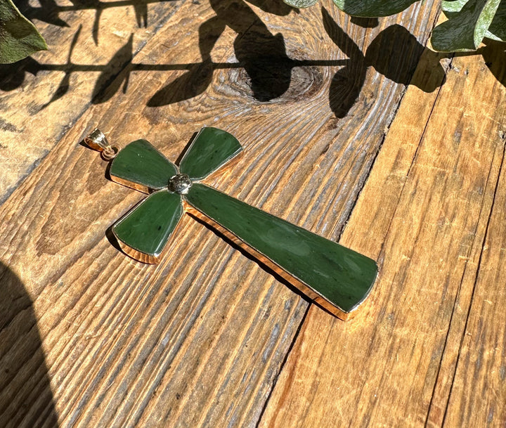 Green jade cross pendant with gold border angled on a wooden table
