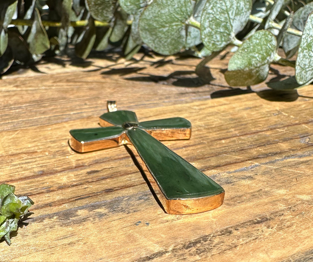Green jade cross pendant with gold trim lying on a wooden surface