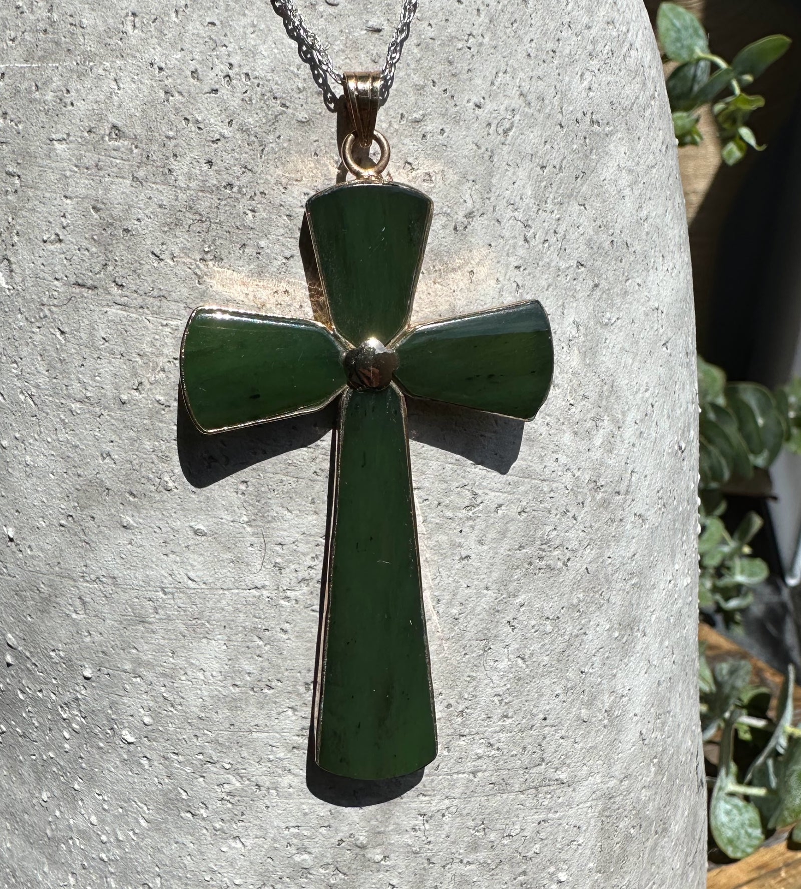 Vintage large jade cross pendant on a silver chain against a stone background