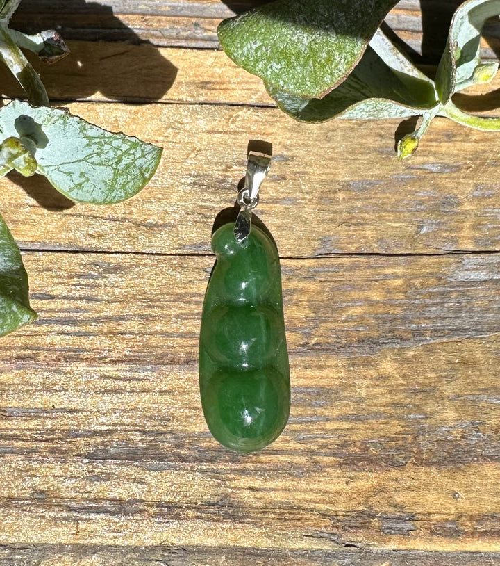 Jade pea pod pendant 25mm with a silver bail on a textured wooden backdrop.