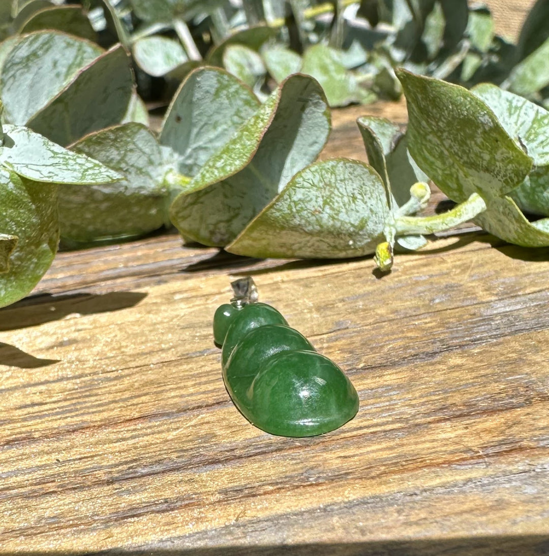 Jade pea pod pendant 25mm with silver bail on rustic wood surrounded by dusty green leaves
