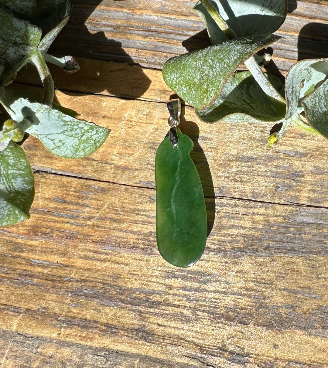 Jade pea pod pendant 25mm with silver bail resting on weathered wood