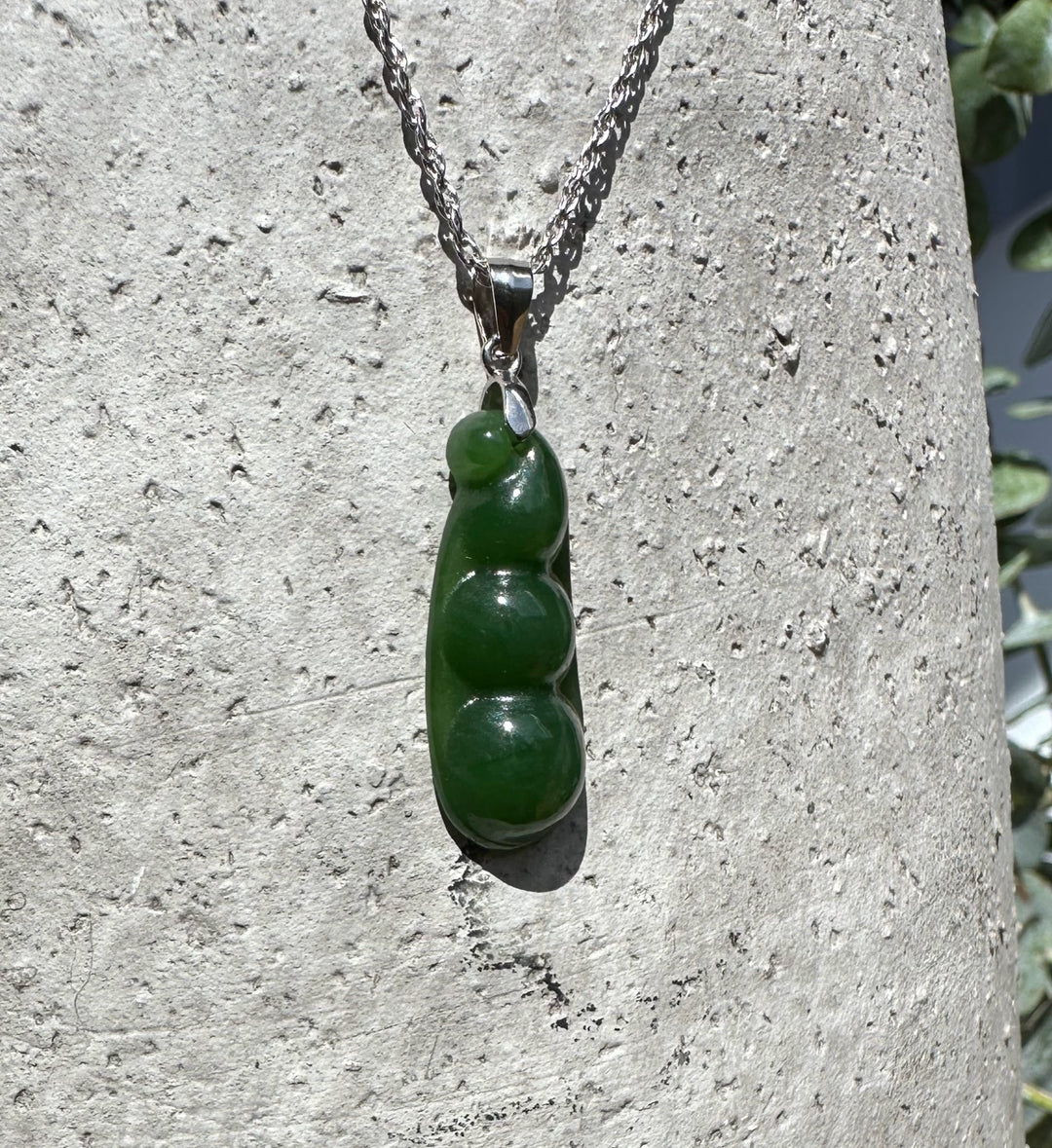 Jade pea pod pendant 25mm on a silver chain against a rough stone background