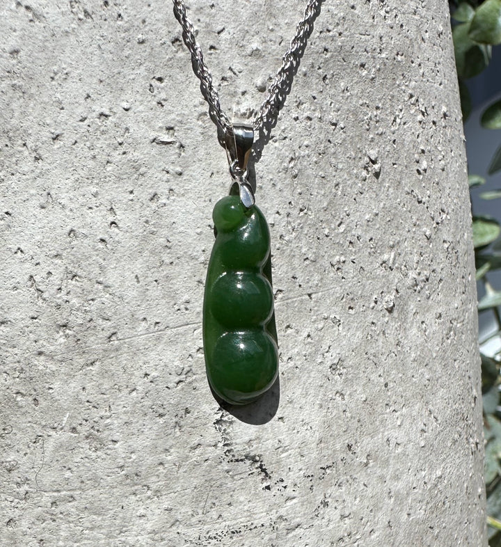 Jade pea pod pendant 25mm on a silver chain against a rough stone background