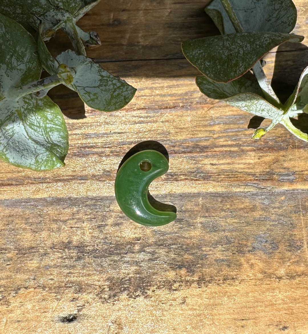 Green jade magatama pendant with a hole near the top laid on wood among leaves