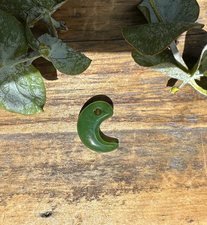 Green jade magatama pendant with a hole near the top laid on wood among leaves