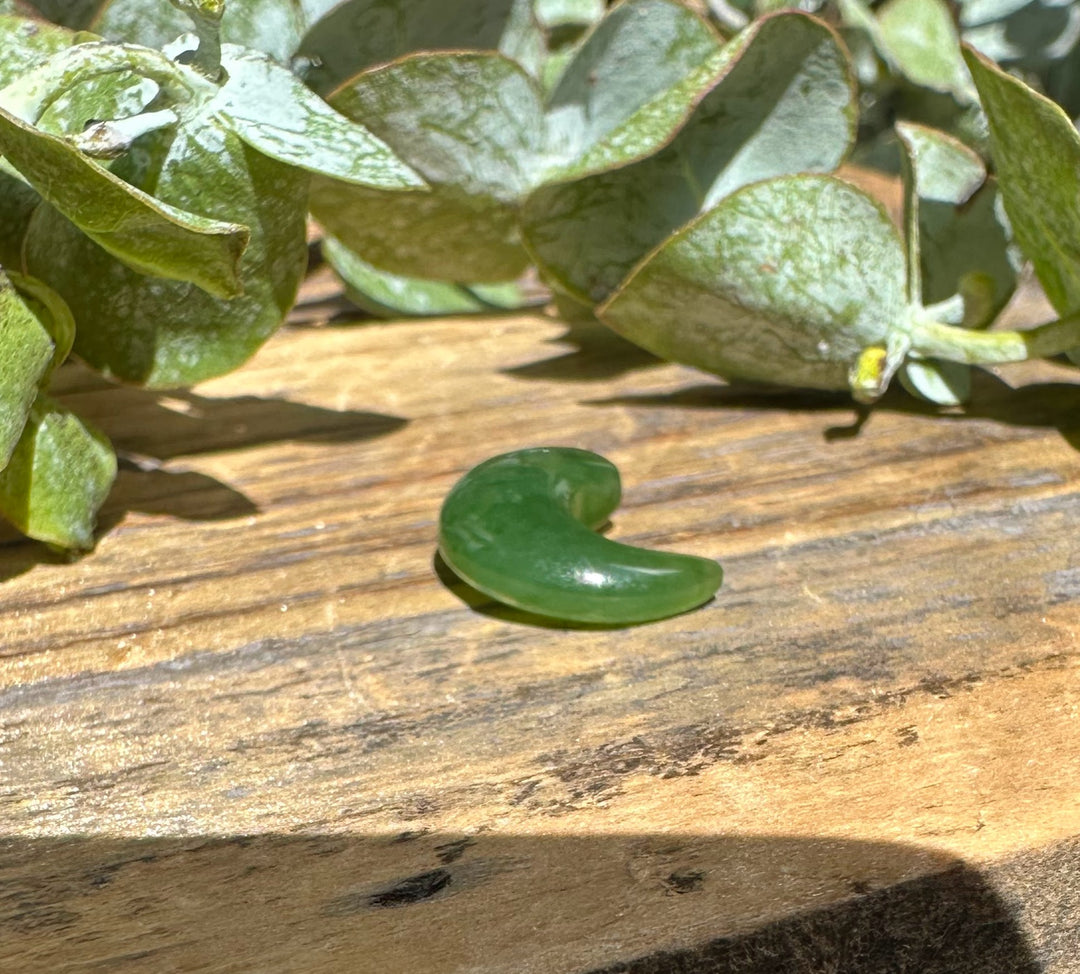 Green jade magatama curved crescent lying on wood with green leaves around.