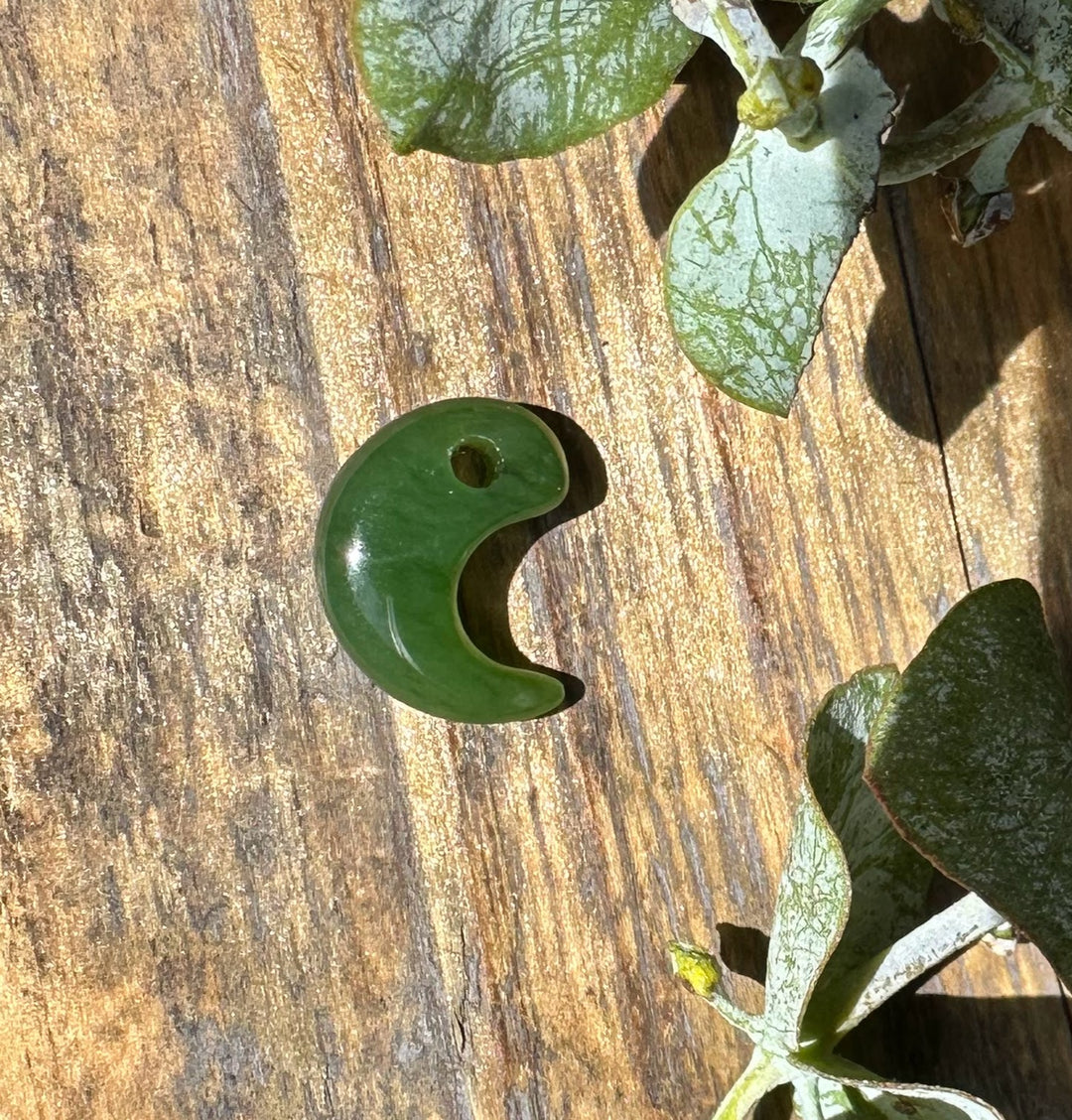 Jade magatama curved crescent bead 12x16mm resting on a wooden surface.