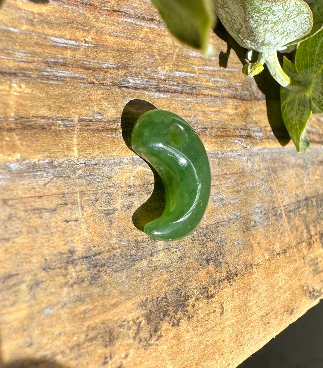 Green jade magatama pendant on a rustic wooden surface with leaves