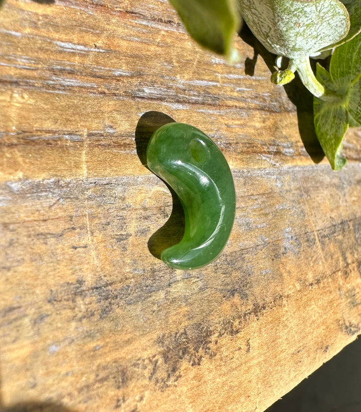 Green jade magatama pendant on a rustic wooden surface with leaves