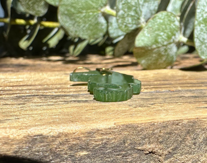 Vintage jade seahorse pendant with a gold bail resting on a weathered wooden surface with leafy greenery in the background.
