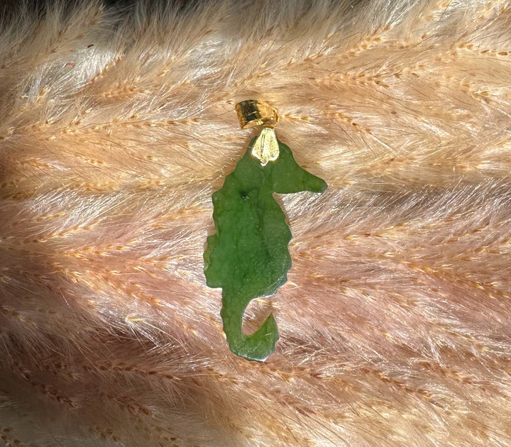 Green jade seahorse pendant with gold bail displayed on soft peach fur background