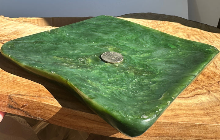 A square green stone or polished wood serving board with rounded corners and a small coin placed on top for scale, resting on a wooden surface.