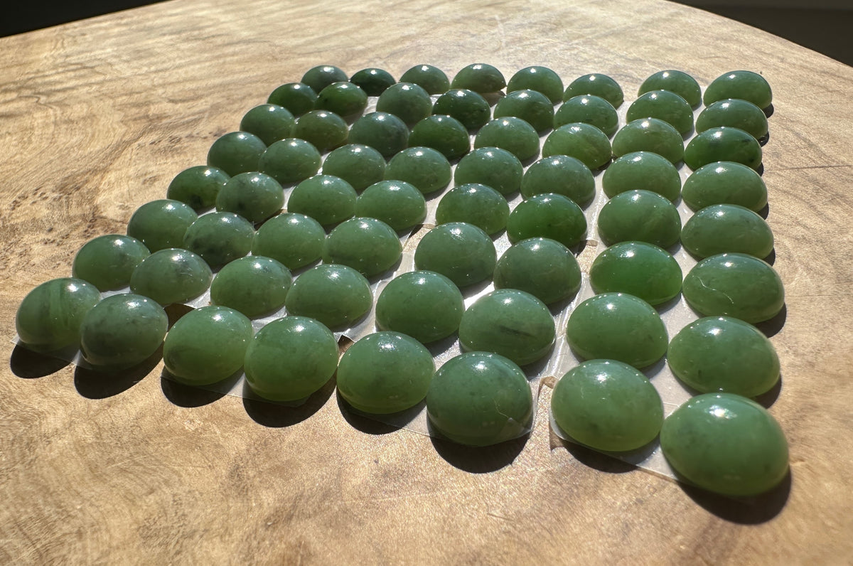 A grid of polished green jade cabs arranged on a clear display sheet, set against a warm wood grain background.