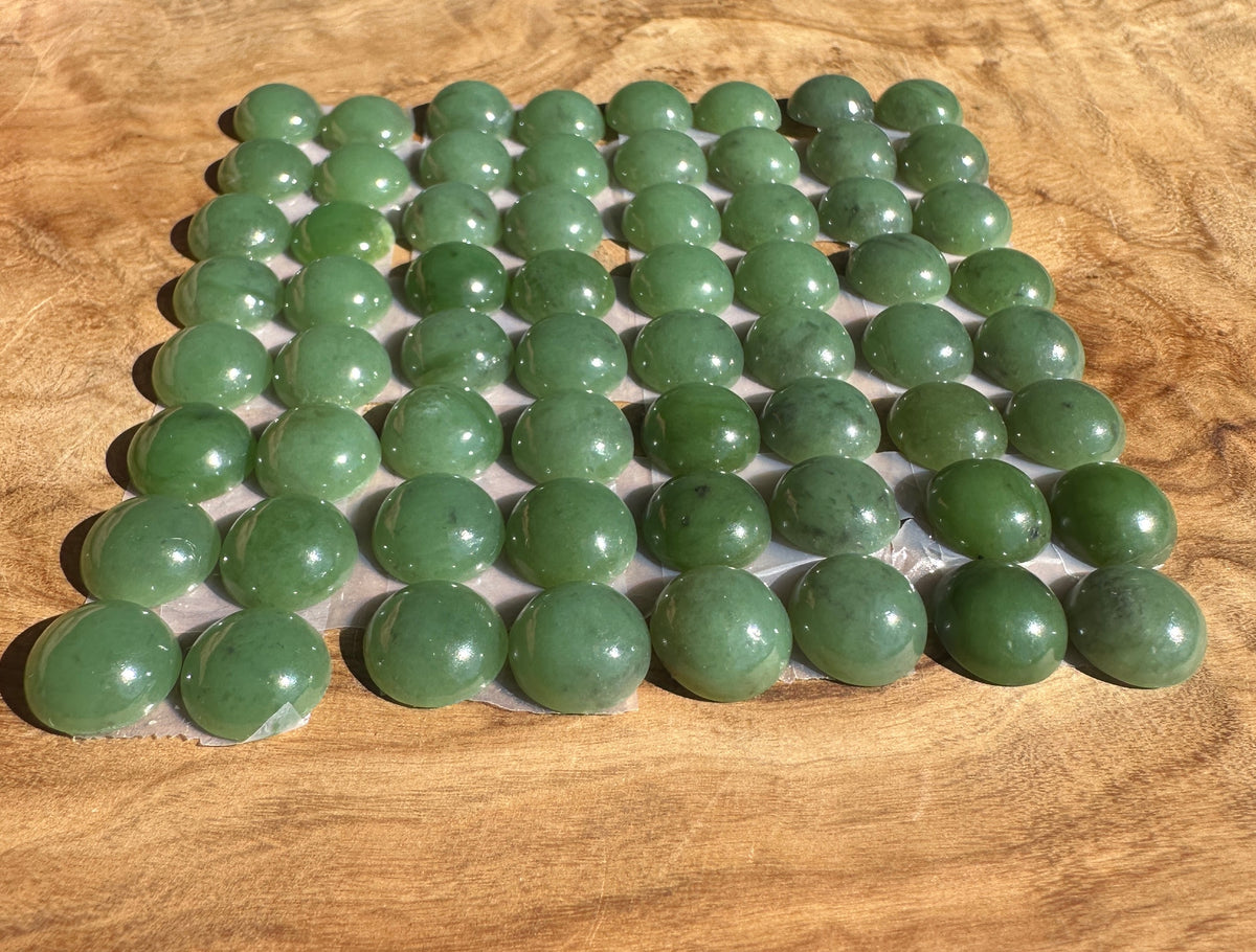 A grid of polished green jade cabs arranged on a clear display sheet, set against a warm wood grain background.