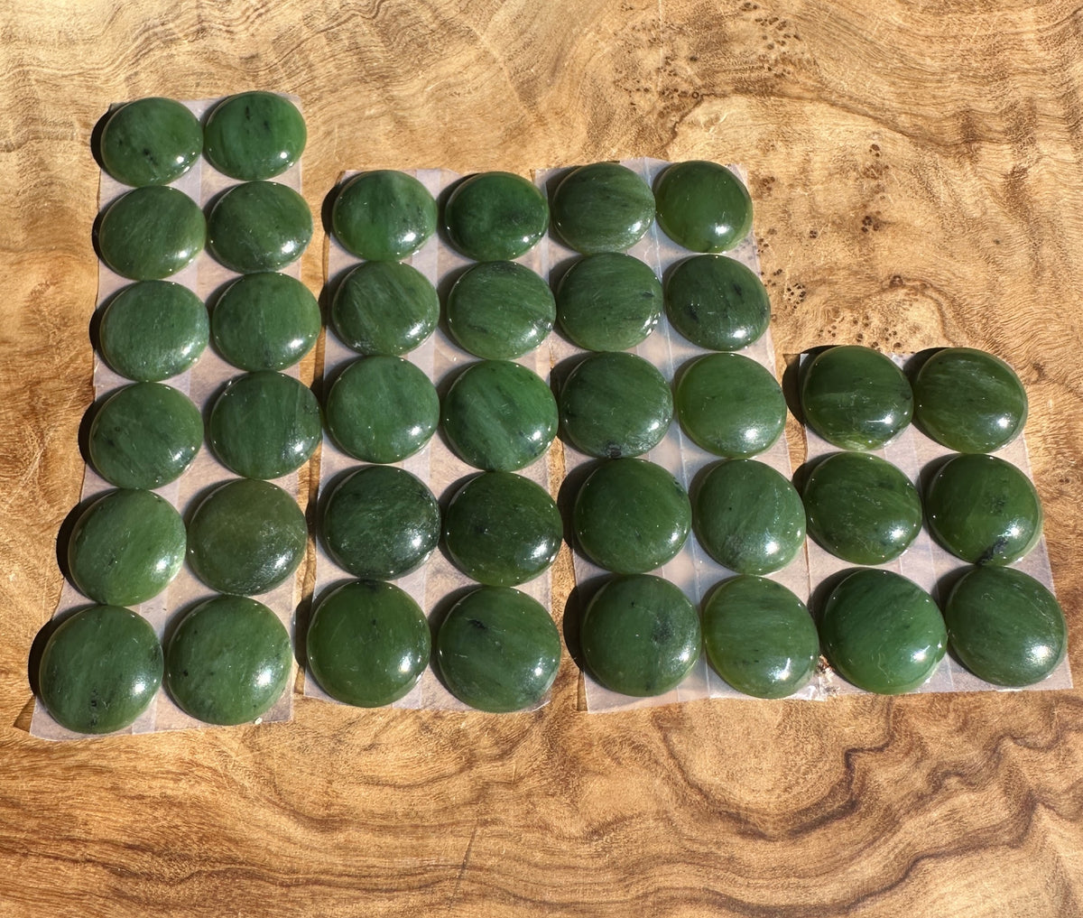 A set of polished dark green jade oval cabochons arranged in rows on a textured wooden background.