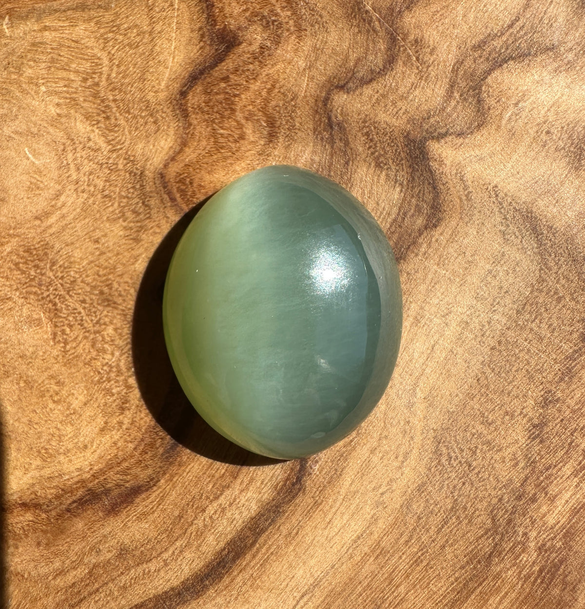 A smooth, polished oval stone with a pale greenish-blue hue resting on a textured wooden surface.