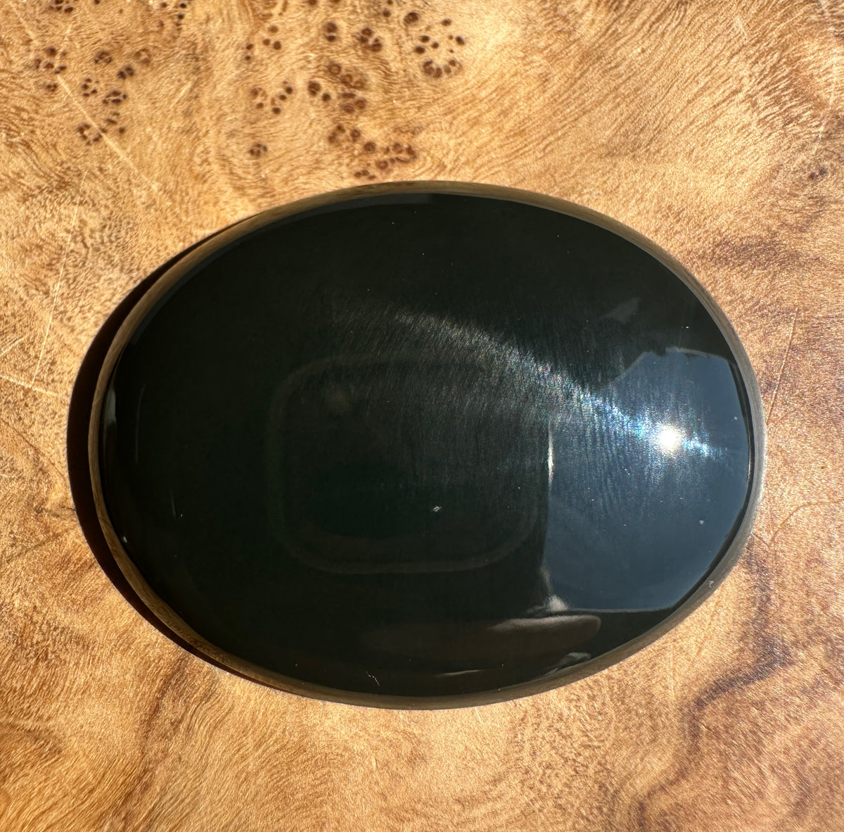 A polished black oval stone cabochon, jade resting on a textured brown wood surface.