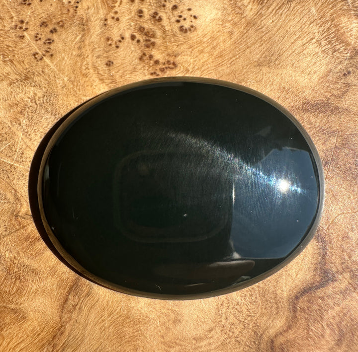 A polished black oval stone cabochon, jade resting on a textured brown wood surface.