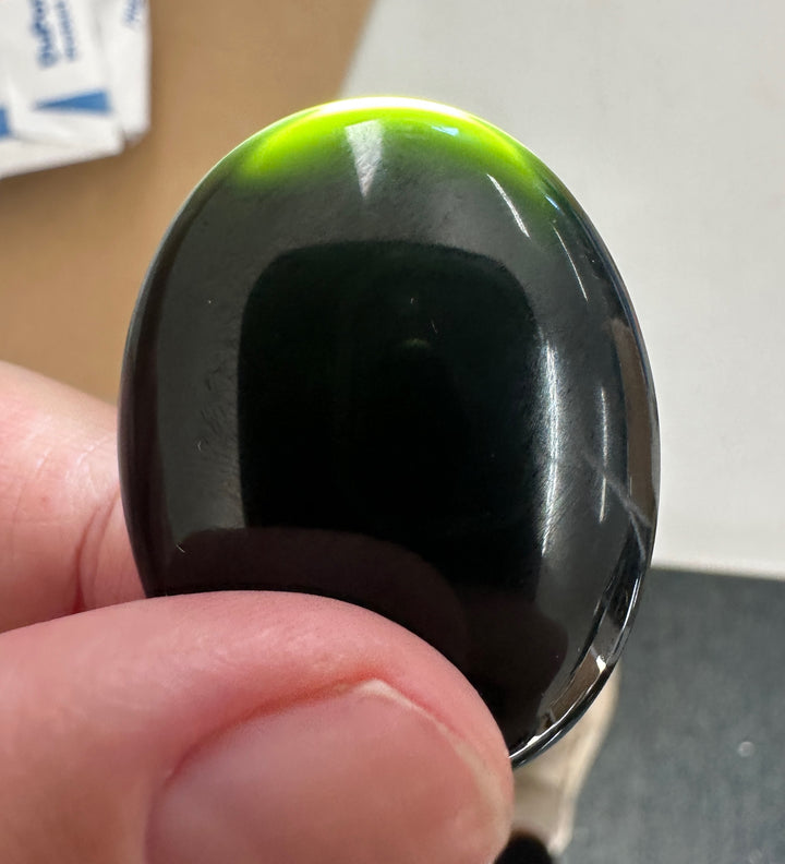 Hand holding a black green jade cabochon, with a bright flashlight behind the jade