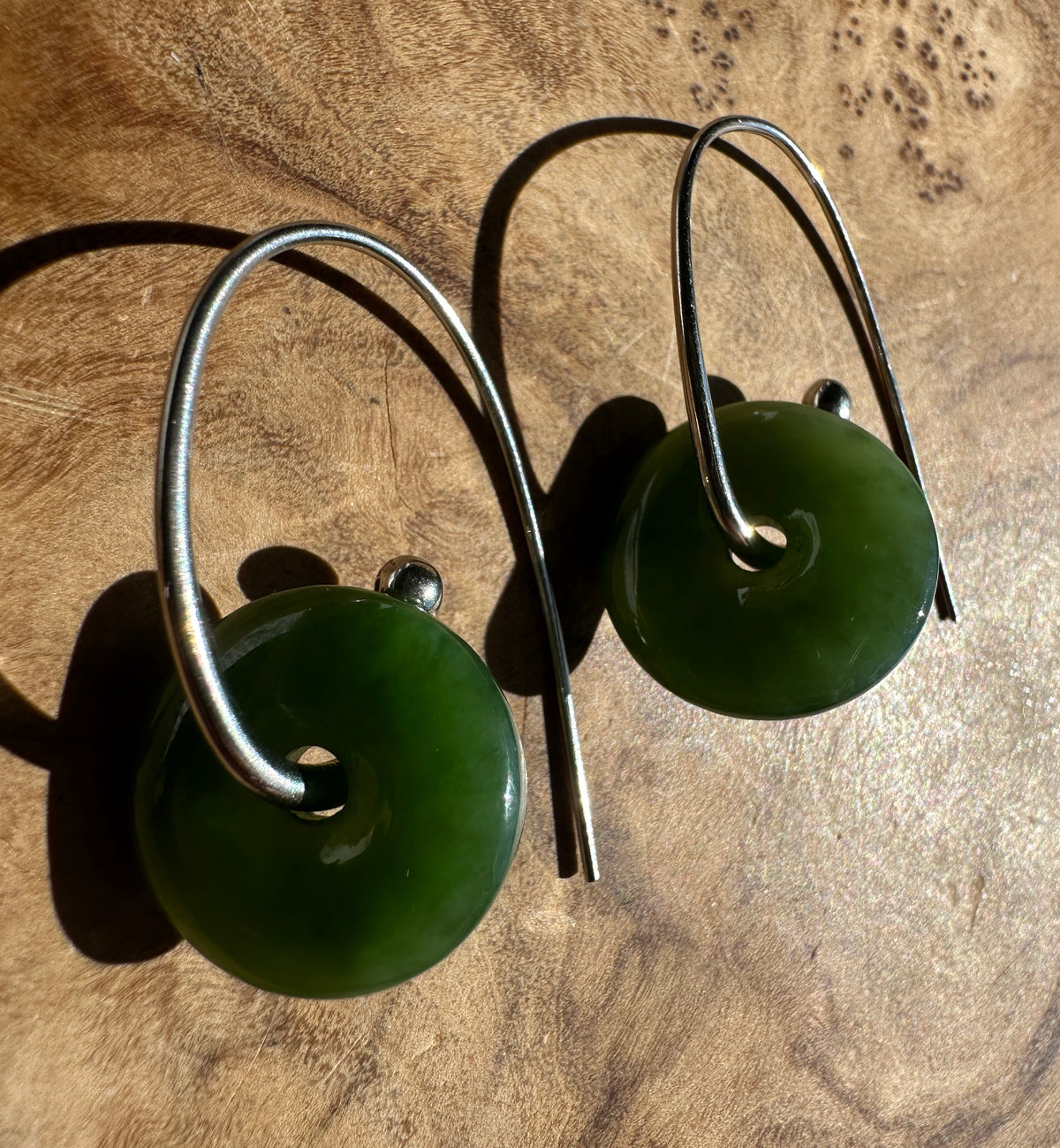 A pair of silver hoop earrings with round green stone pendants, displayed on a textured wooden surface.
