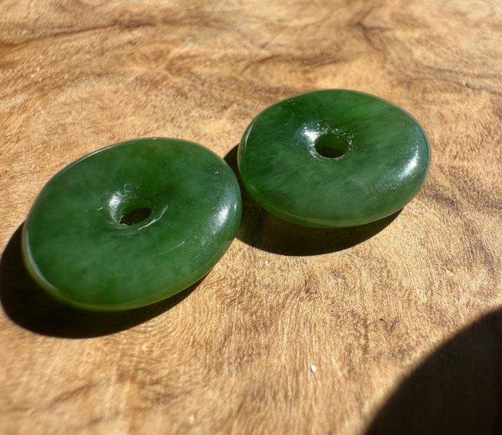 Two green jade wedge-shaped pendant beads) resting on a textured wooden surface under direct sunlight.