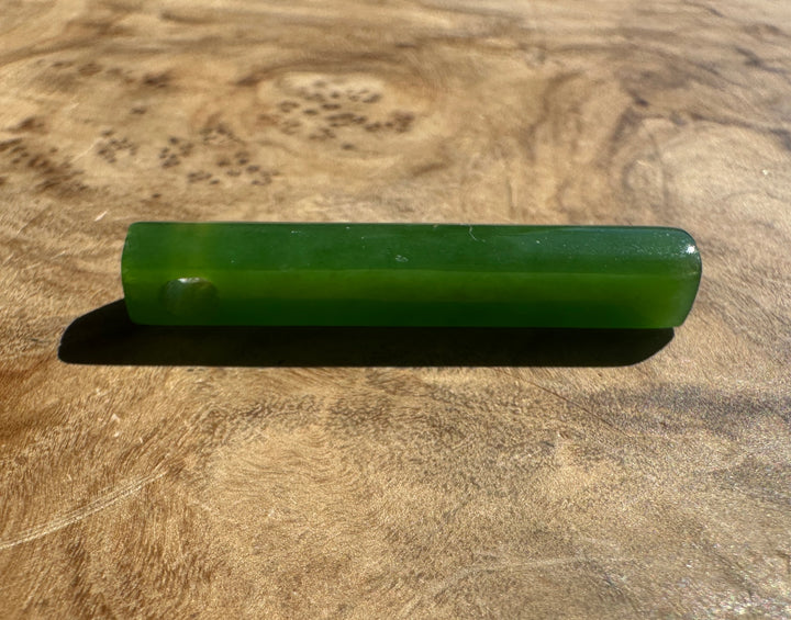 A green polished stone pendant, resting on a textured wooden surface.