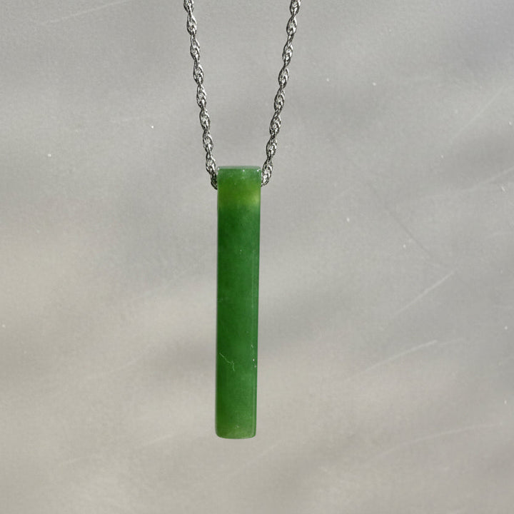 Bright Green jade pendant hanging on a silver chain. Grey background