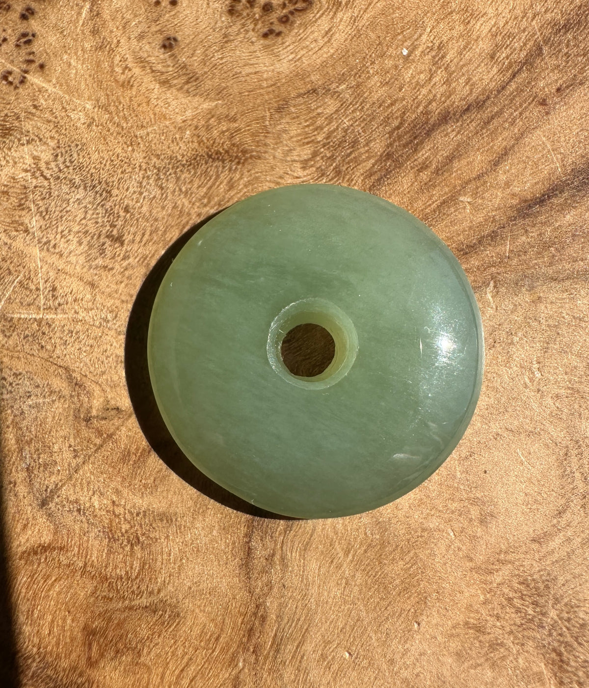 A round light green jade pendant with a central hole, resting on a textured wooden surface.