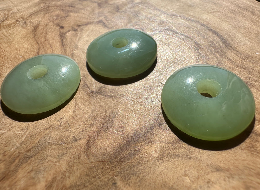 Three round light green jade disc beads with central holes, displayed on a textured wooden surface.