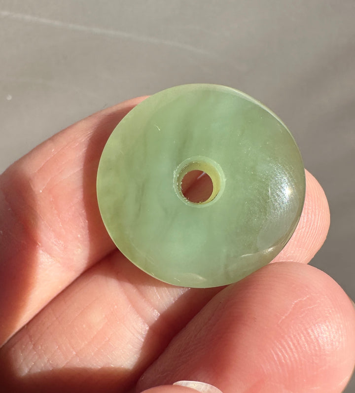 A light green jade disc pendant with a central hole, held in a person&
