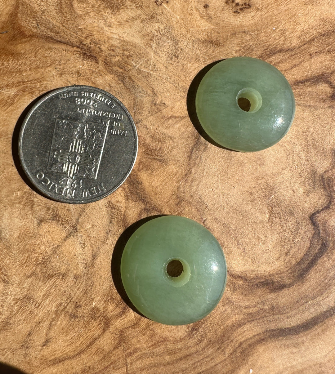 Two round light green stone beads with central holes, shown on a wood surface next to a U.S. quarter for scale.