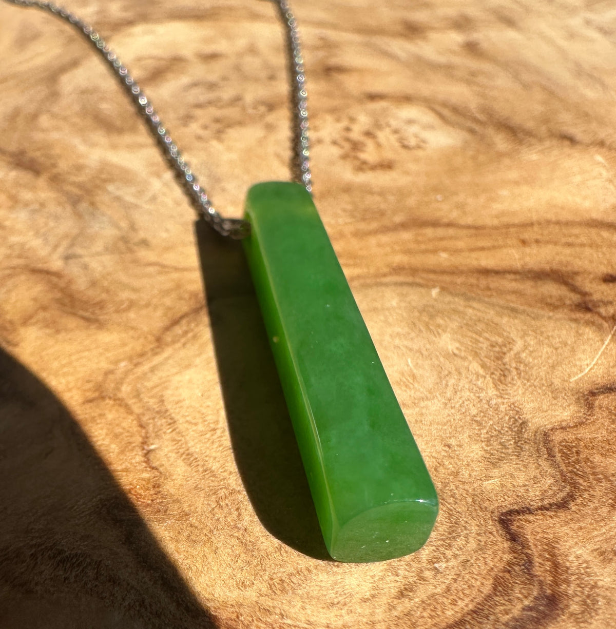 A green polished stone pendant necklace on a silver chain, resting on a textured wooden surface.