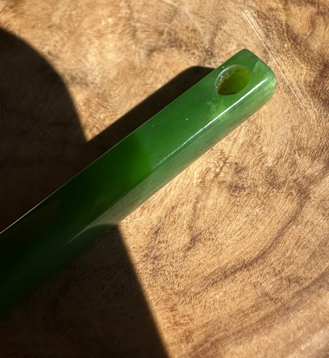 Close up of jade, showing the hole and internal flaws, sitting on a wooden surface