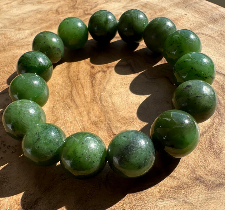 A beaded bracelet made of polished green jade-like round beads, arranged in a circle on a wooden surface.