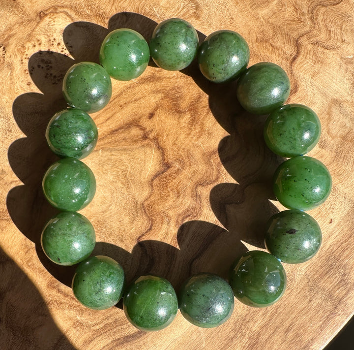 A beaded bracelet made of polished green jade-like round beads, arranged in a circle on a textured wooden surface.