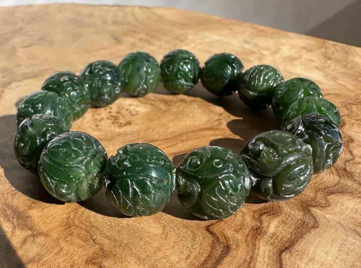 A beaded bracelet made of carved dark green jade-like round beads, displayed on a textured wooden surface.