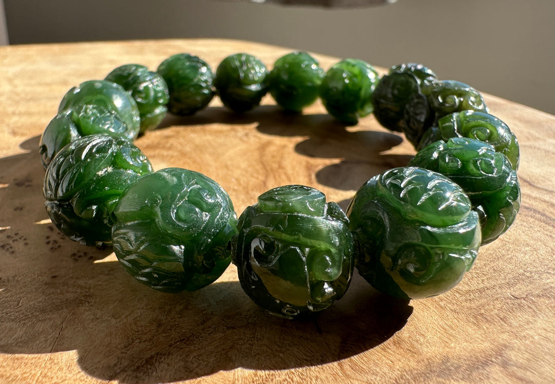 A beaded bracelet made of carved dark green jade-like round beads, displayed on a textured wooden surface.