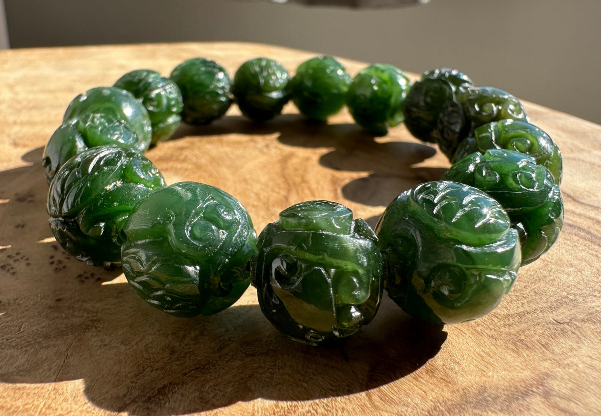A beaded bracelet made of carved dark green jade-like round beads, displayed on a textured wooden surface.