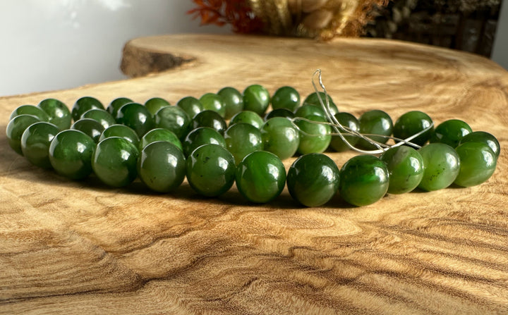 Unstrung 10mm green jade beads resting on a wooden surface with a loose string