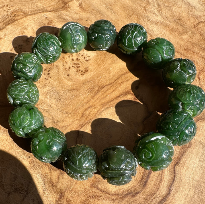 A beaded bracelet made of carved green jade-like round beads, arranged in a circle on a natural wood surface.